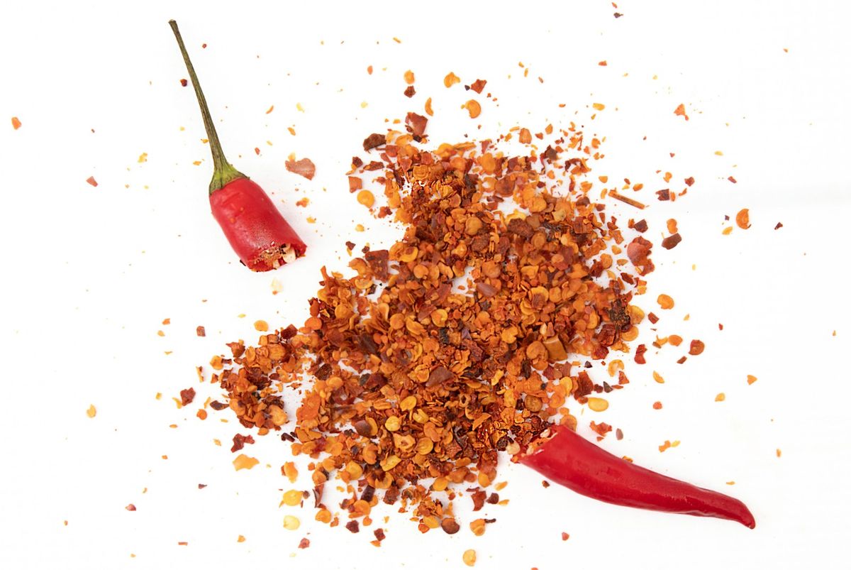 Chiliflakes bredvid en röd chilipeppar
